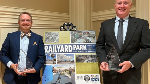 Two men holding awards and standing next to a poster showcasing Railyard Park.